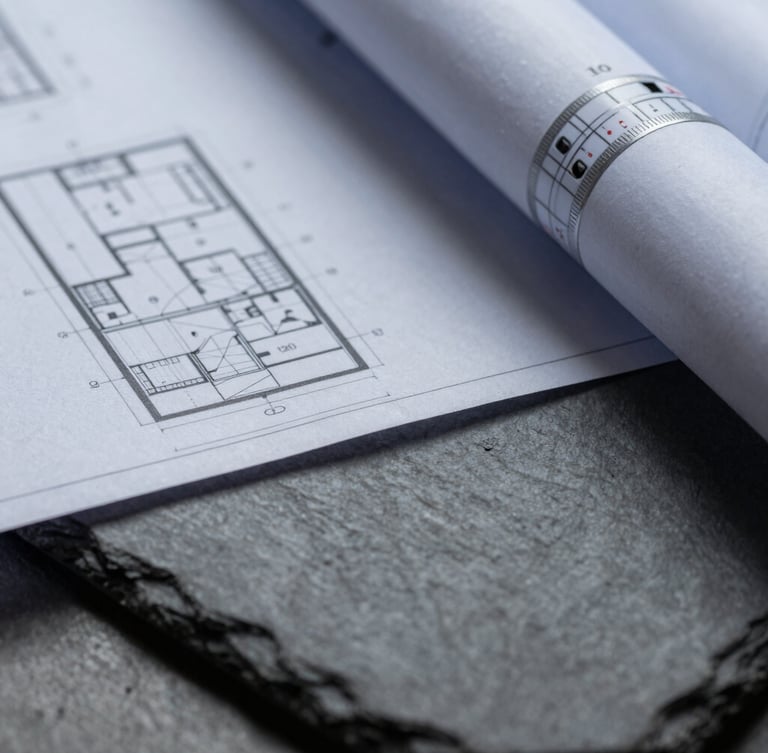 A close-up macro shot of architectural blueprints resting on a dark slate surface, sharp shadows, cool diffused daylight.