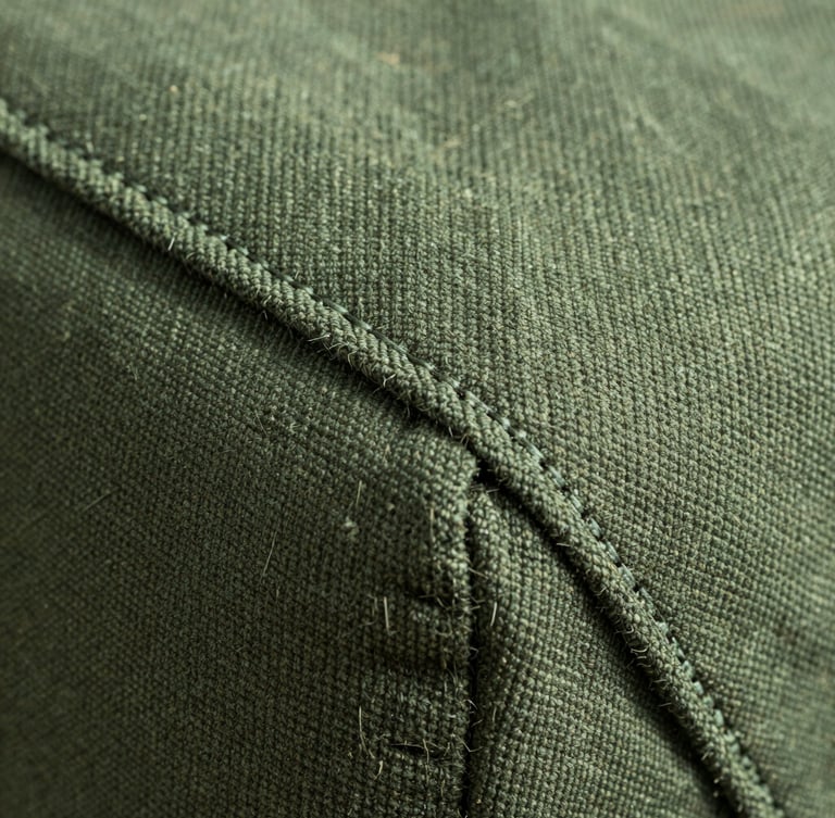 Extreme macro shot of heavy-duty pine green canvas fabric, showing rugged double-stitch seams and natural fiber texture under crisp morning light.