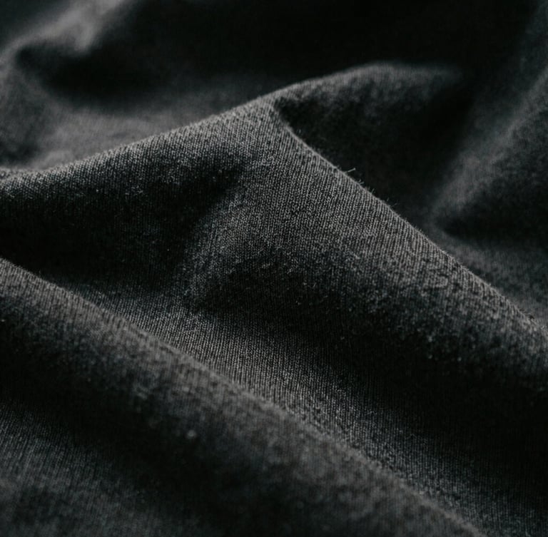 Macro close-up of 280gsm organic cotton knit texture, high-contrast directional light, deep shadows, desaturated dark tones, 35mm film grain