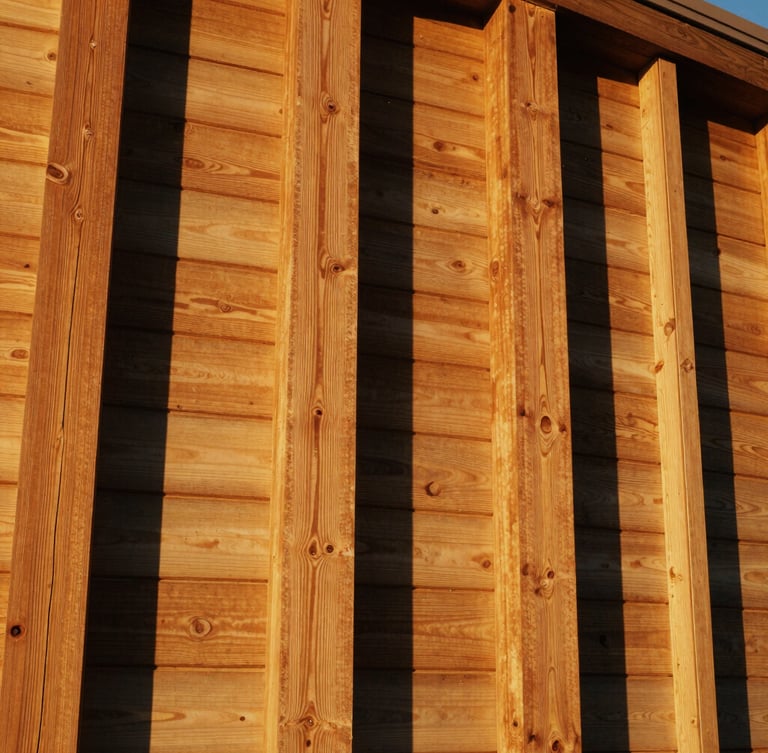 Low-angle architectural shot showing structural alignment of redwood posts and horizontal boards, warm golden-hour California sunlight, rich golden-brown wood tones, 35mm