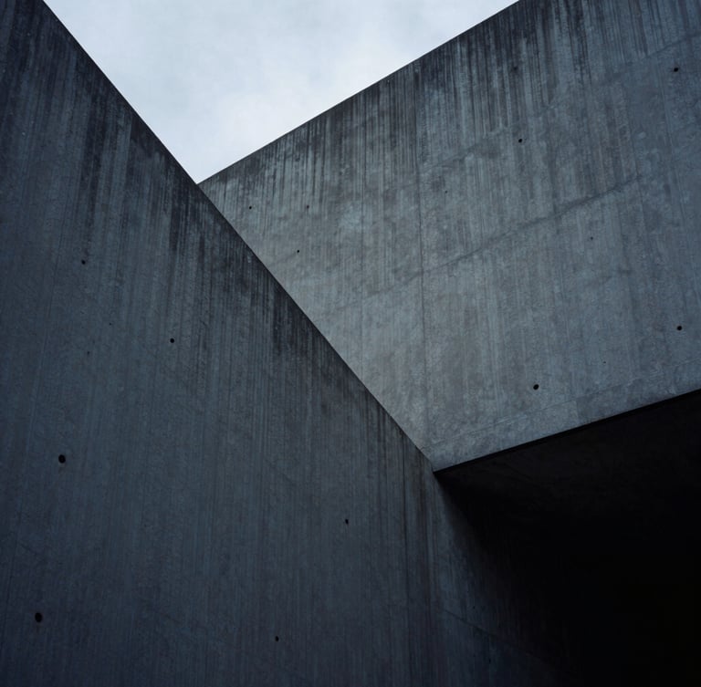 Low-key cool-toned photograph of sharp concrete architectural angles, deep shadows, overcast diffused daylight, 35mm