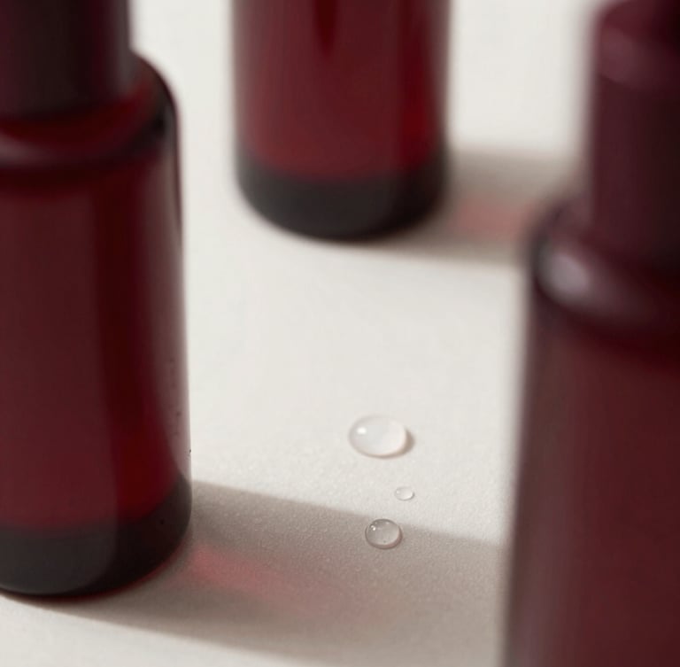 Close-up of elegant product bottles styled alongside clean water droplets and soft shadows, minimalist editorial photography, soft natural side-light, deep burgundy tones, macro lens detail.