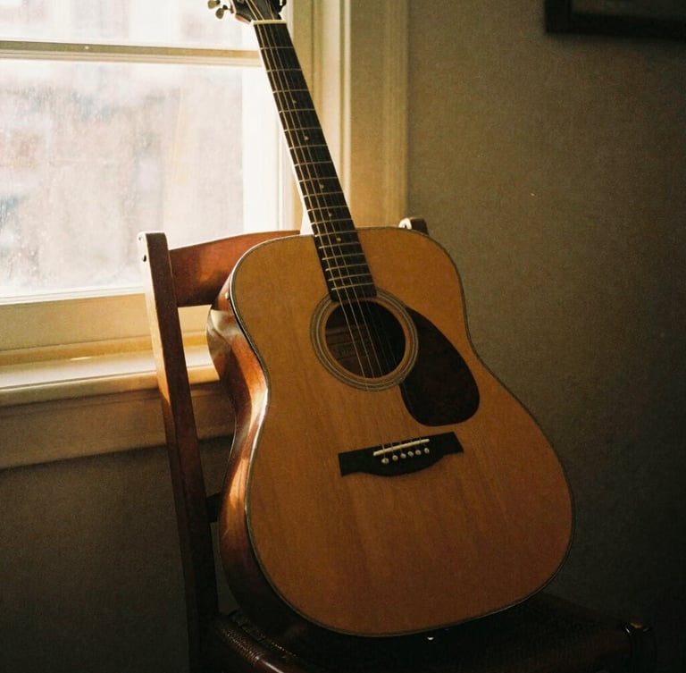 Warm vintage film photography of a worn acoustic guitar leaning against a wooden chair, dusty golden-hour light streaming through a window, 35mm grain.
