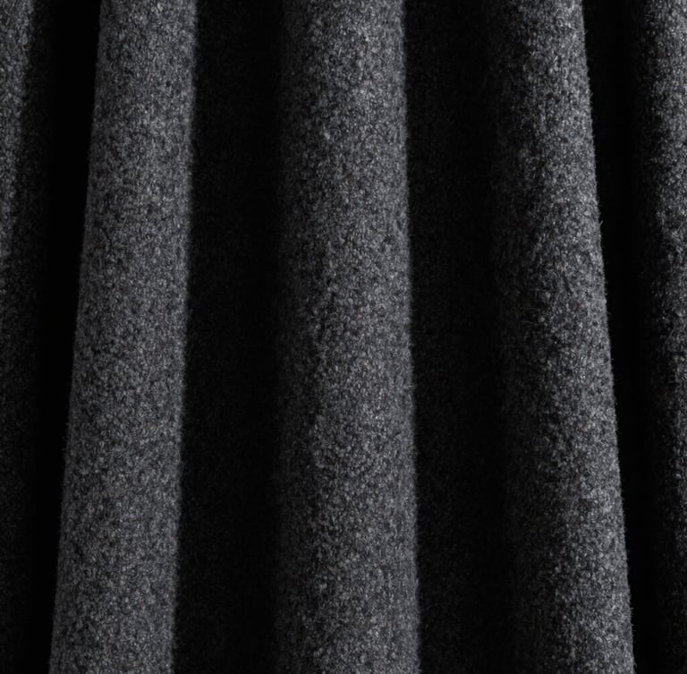 Extreme close-up of heavy structured charcoal wool drape, sharp directional studio light, deep shadows, high-contrast minimalist editorial fashion photography