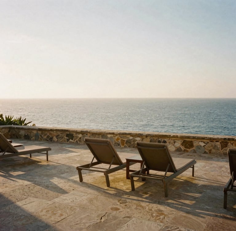 Serene sun-drenched stone terrace overlooking the Mediterranean sea at golden hour, empty elegant lounge chairs, warm side-light, editorial luxury travel photography, 35mm film aesthetic