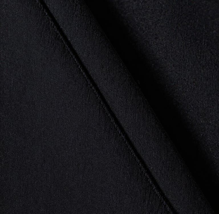 Extreme macro close-up of heavy black cotton fabric weave, showing sharp architectural seam detail, stark high-key studio lighting, desaturated monochromatic tones.