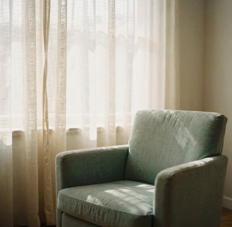 Warm editorial photography of a peaceful consulting room, soft morning window light filtering through linen curtains, comfortable sage green armchair, warm sand tones, shallow depth of field, 35mm film