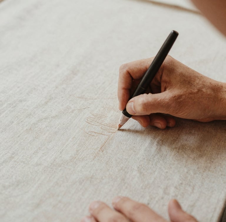 Close-up of hands chalking a pattern on heavy neutral linen, soft diffused natural daylight, warm undertones, editorial fashion lookbook style, 35mm film