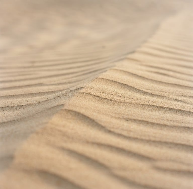 Minimalist macro photography of soft sand ripples, gentle morning shadows, warm sand tones, clean composition, high negative space, quiet contemplative mood.