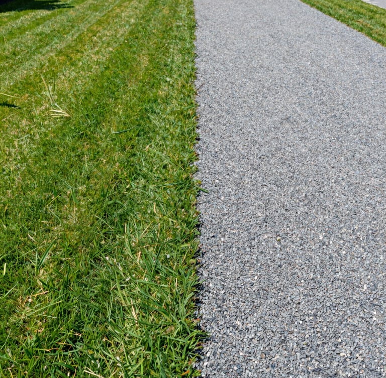 Wide environmental shot of a pristine, freshly cleared property line, sharp green lawn on one side, slate gray gravel path on the other, bright direct natural daylight, 35mm