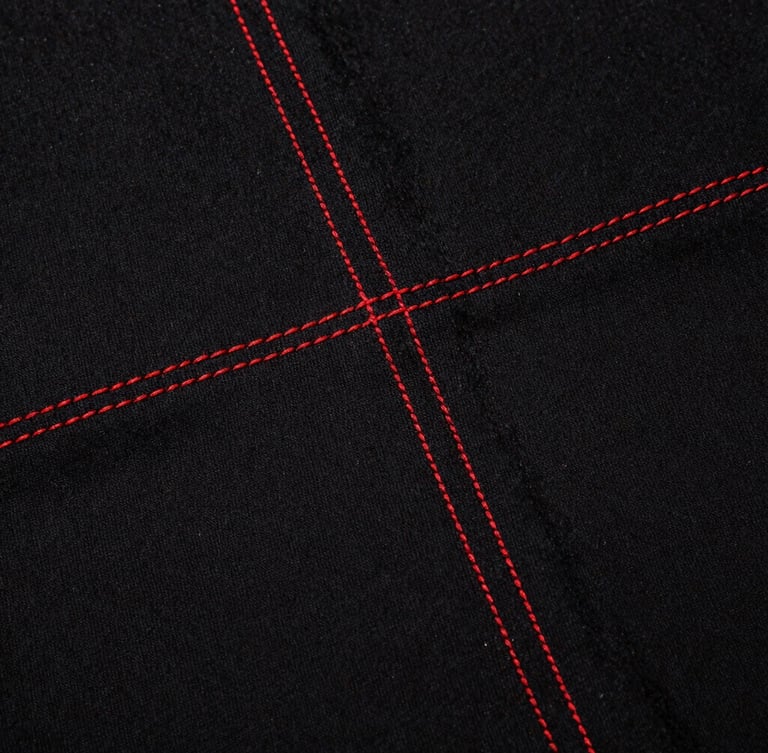Gritty close-up texture shot of heavyweight black cotton fabric with raw red stitching, direct flash, high contrast, harsh shadows