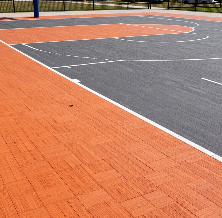 Sharp architectural sports photography of a freshly completed outdoor basketball court with orange and charcoal PP interlocking tiles, bright crisp daylight, wide-angle lens