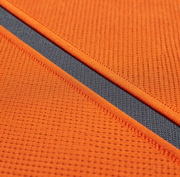 Macro shot of high-contrast orange and charcoal sublimated athletic fabric under stadium floodlights, showing precise stitch lines and vibrant mesh texture.