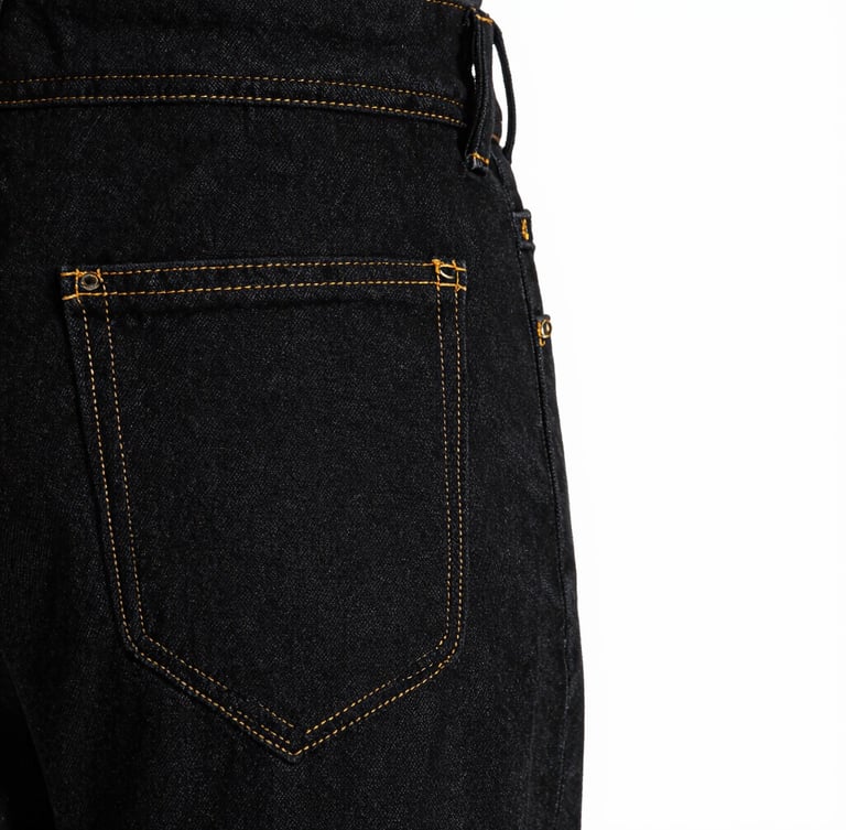 Tight macro crop of garment construction, golden stitching on premium black denim fabric, high-contrast studio lighting, sharp focus on seams