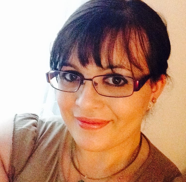ophelie bottin: A smiling woman with bangs wearing stylish rectangular glasses and a necklace.