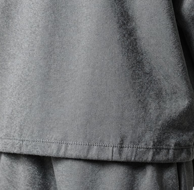 Extreme close-up of heavy-weight cotton fabric texture, double-stitched hem details, cold overcast studio lighting, desaturated grey tones, high-contrast.