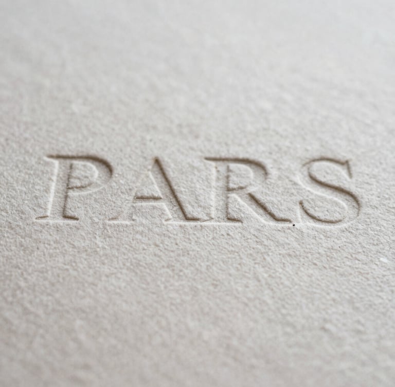 Macro photograph of heavy textured cotton paper with debossed typography, soft shadows, natural overcast Parisian light, editorial film style
