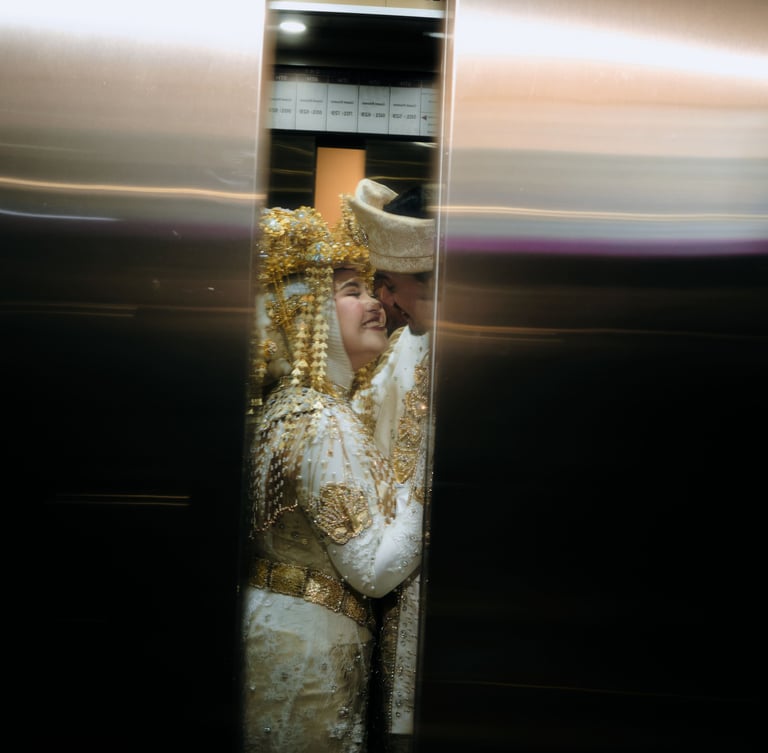 A smiling couple in traditional white and gold wedding attire glimpsed through closing elevator doors.