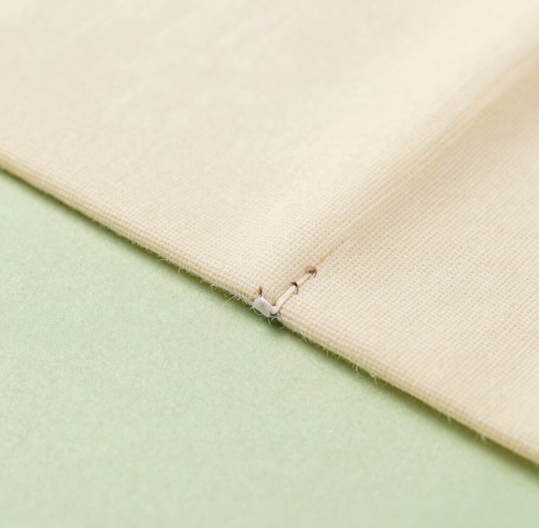 Macro detail shot of a clean ultrasonic weld seam on a raw canvas cream nonwoven bag, showing fused spunbond fabric texture, soft industrial studio lighting