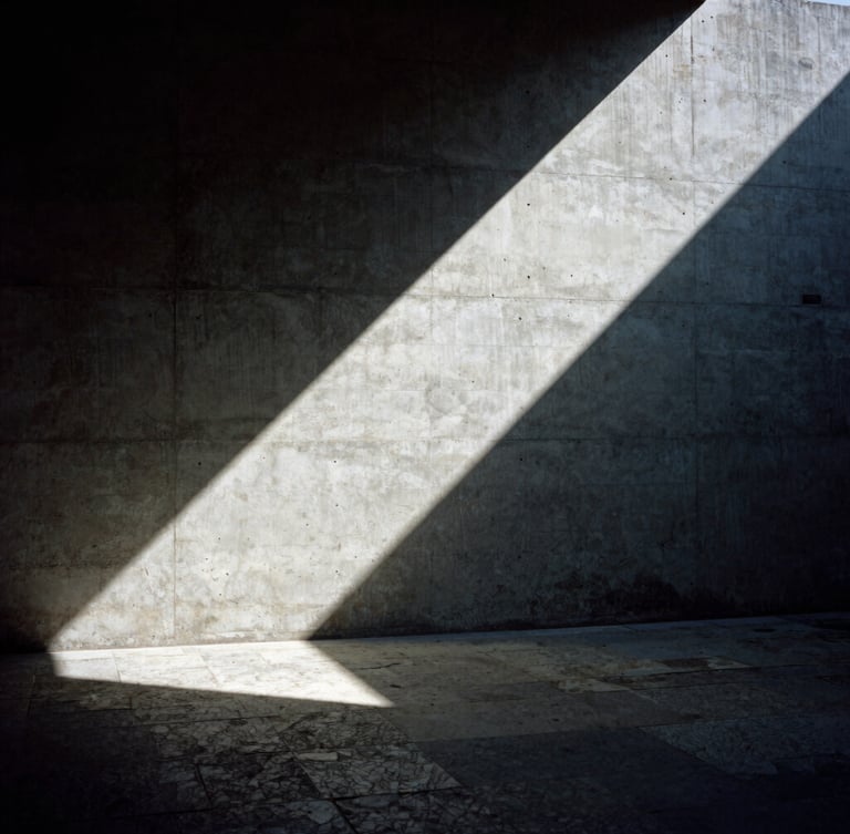 Dramatic architectural photography of an interior concrete wall meeting a rough-hewn stone floor, stark directional sunlight casting deep diagonal shadows, 35mm film.