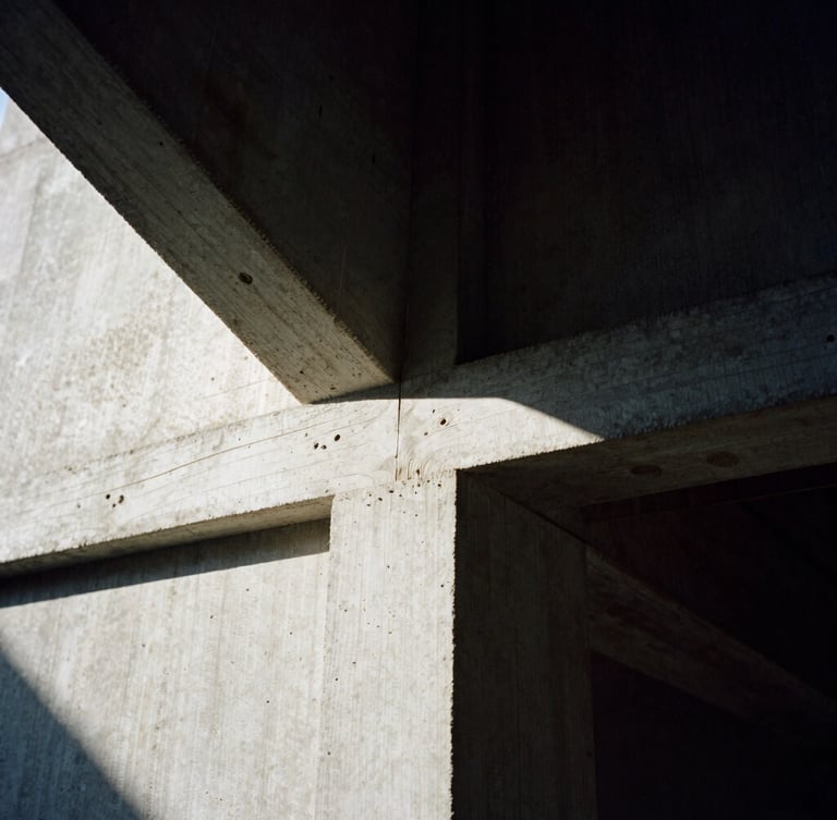 Macro detail of hand-carved wood joint meeting raw textured concrete, deep architectural shadows, strong directional sunlight, high-contrast chiaroscuro, 35mm film