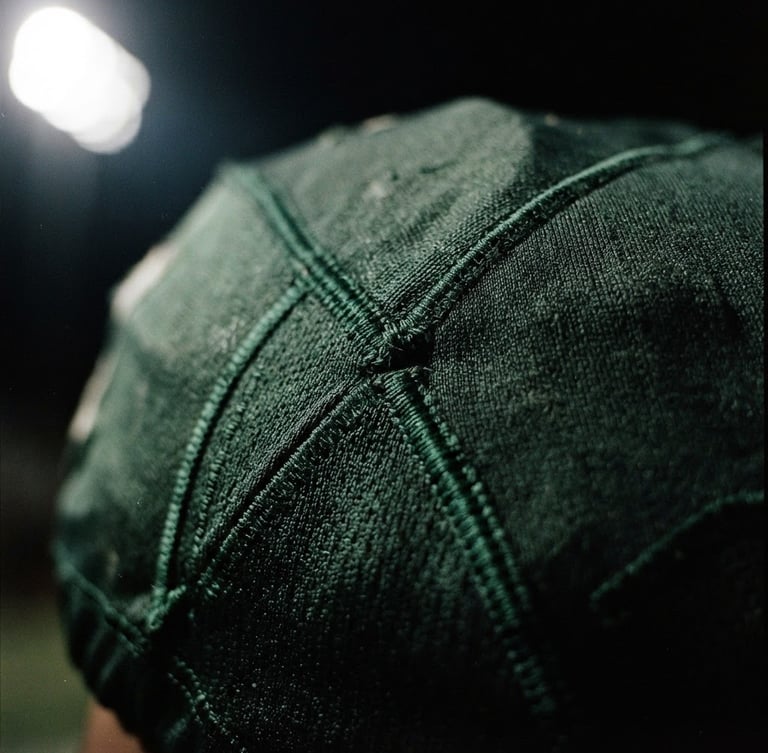 Close-up of a premium textured football jersey fabric with deep green stitching under dramatic stadium floodlight illumination, high-contrast 35mm film