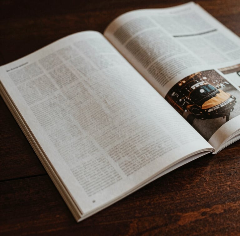 Close-up of tactile printed magazine pages on a dark wooden desk, natural high-contrast side lighting, deep rich tones, 35mm film style.