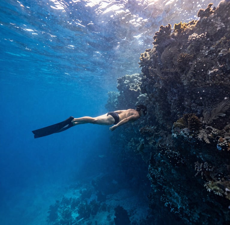 Wide-angle shot of a diver in perfect horizontal trim drifting along a deep blue vertical reef wall in Cozumel, sunbeams piercing the crystal clear water