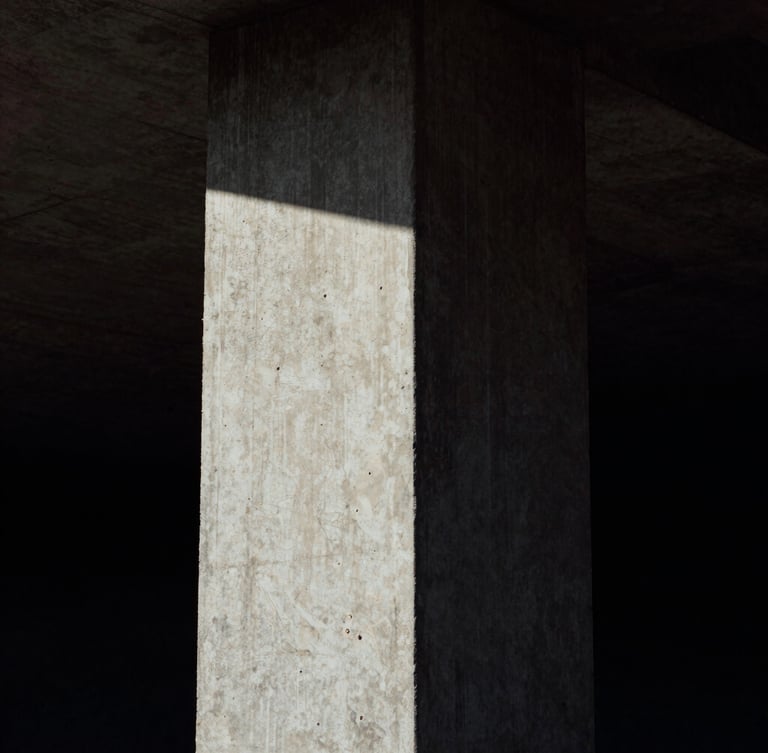 High-contrast portrait of a brutalist concrete column under dramatic low-key natural light, deep shadows, raw concrete texture, medium-format film grain, dark atmospheric photography