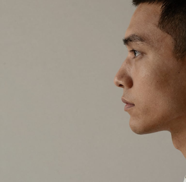 Minimalist studio portrait of a male designer, side profile, warm clay-toned lighting, soft diffused drop shadows, neutral desaturated background, sharp macro lens composition.
