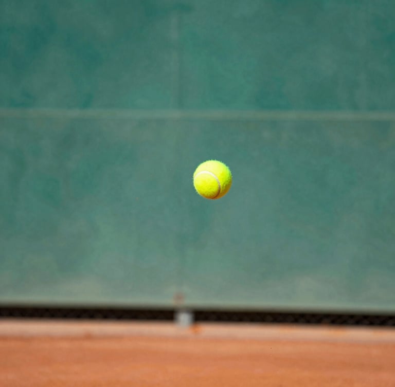 Dynamic close-up action shot of a tennis racket hitting a yellow tennis ball mid-air, red clay dust exploding from the impact, bright sunny afternoon lighting, shallow depth of field.