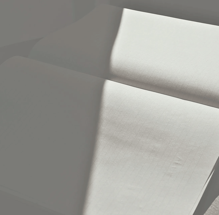 An open, lined notebook captured in a minimalist play of sharp sunlight and deep shadow.