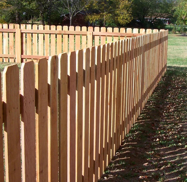 A classic natural cedar wood dog ear picket fence installed around a backyard lawn.