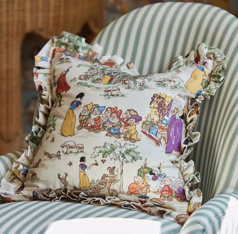 Un coussin aux motifs des sept nains et blanche neige, posé sur un fauteuil à rayures