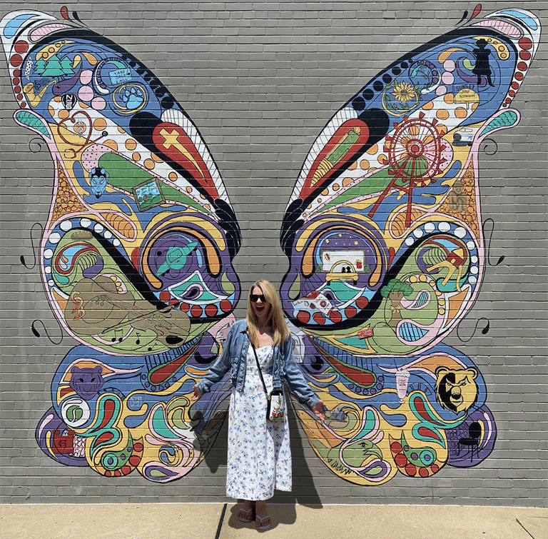 Nini standing against a wall with a mural of butterfly wings