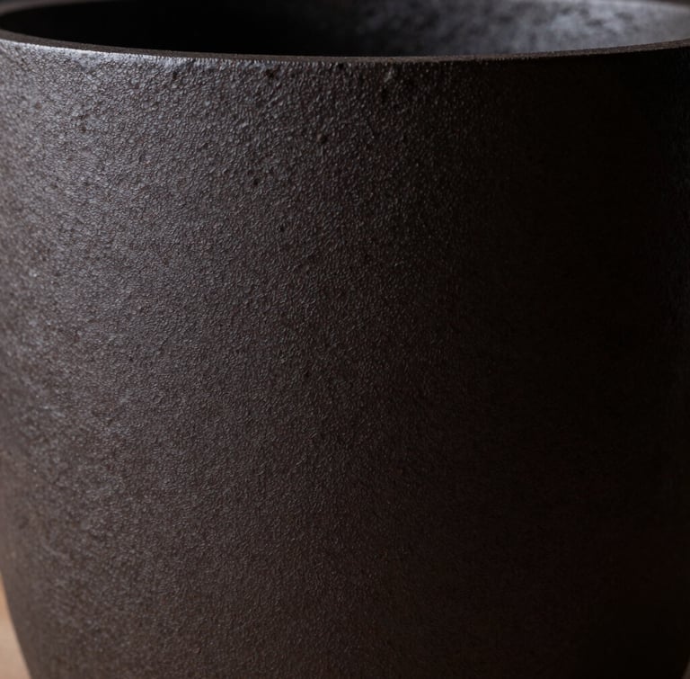 Extreme close-up of a dark, matte cast iron vessel, a single shaft of light revealing its rough, porous texture, deep shadows, minimalist fine art aesthetic.