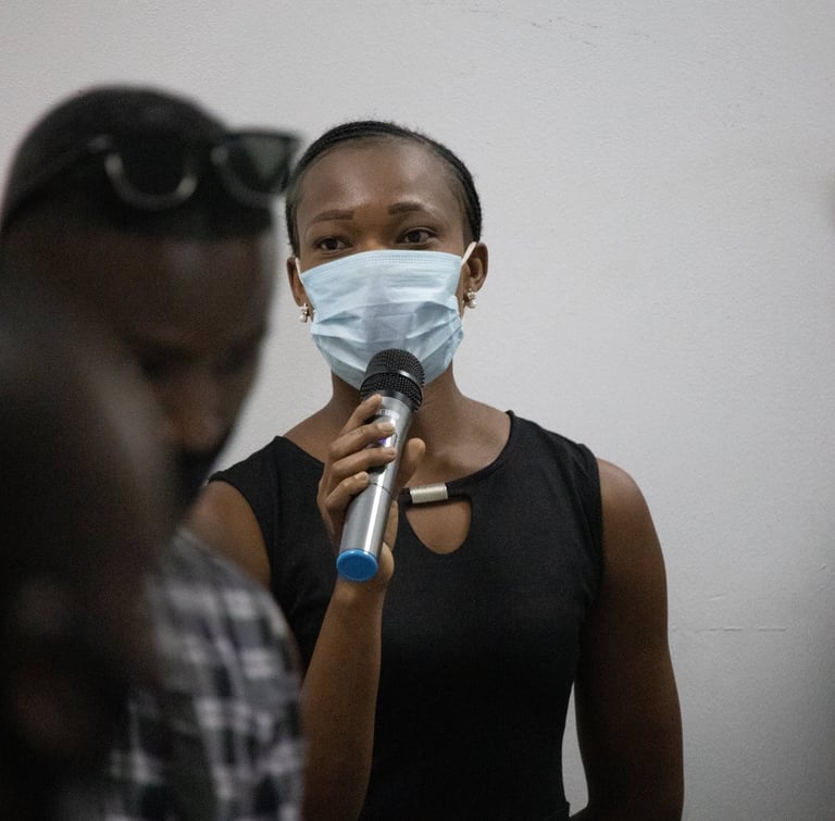 a woman in a black dress and face mask speaking into a microphone