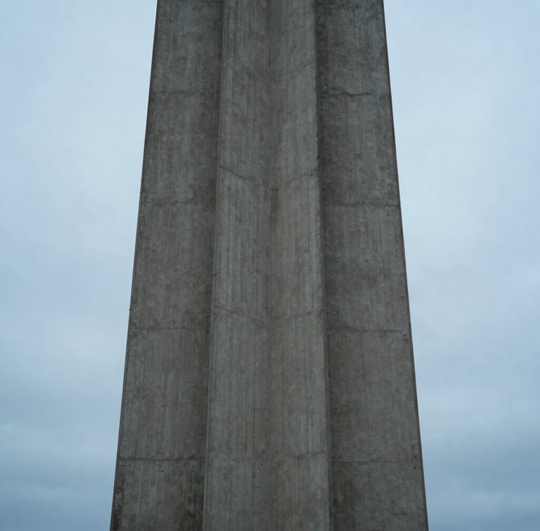 A tall architectural structure on Bainbridge Island, clean concrete lines meeting an overcast sky blue horizon, diffused cool light, portrait orientation.