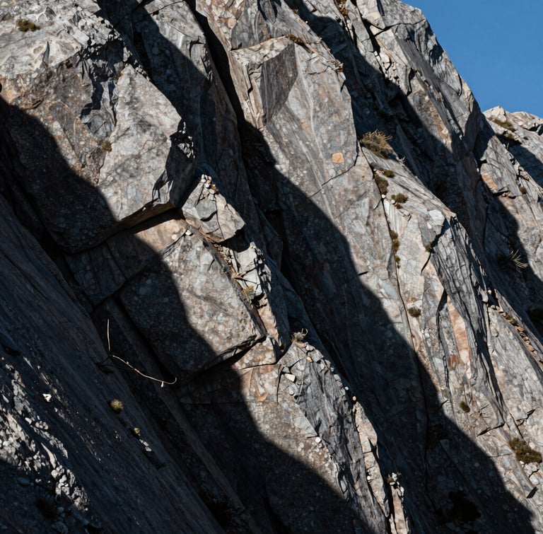 Stark, high-contrast mountain light casting deep shadows on raw stone blocks, architectural composition, portrait orientation.