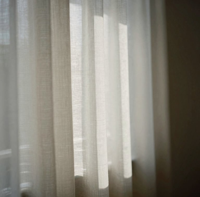 A portrait crop of soft diffused morning light filtering through structured linen fabric, casting gentle shadows, quiet studio corner, minimalist composition