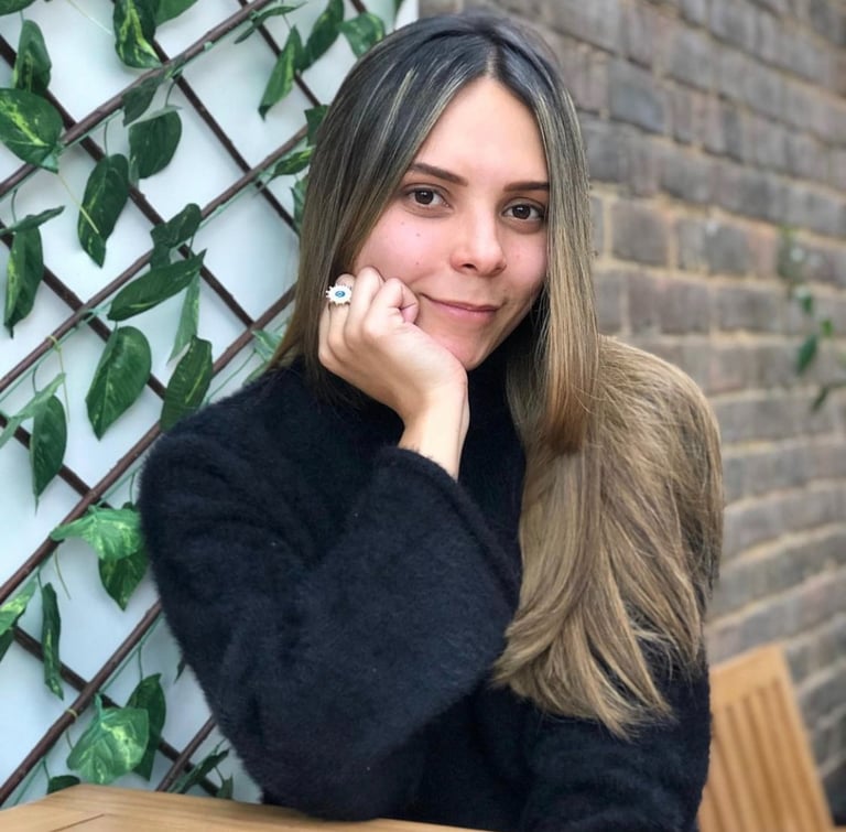 una mujer sonriendo a la camara sutilmente con su mano sosteniendo su cara