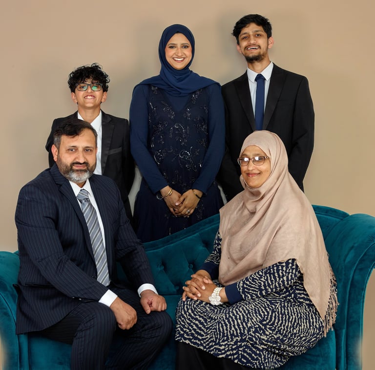 A smiling Muslim family in formal attire and hijabs posing for a studio portrait on a blue sofa.