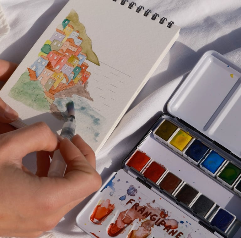 Un artiste réalise une aquarelle représentant des maisons de village côtier dans un carnet de croqui