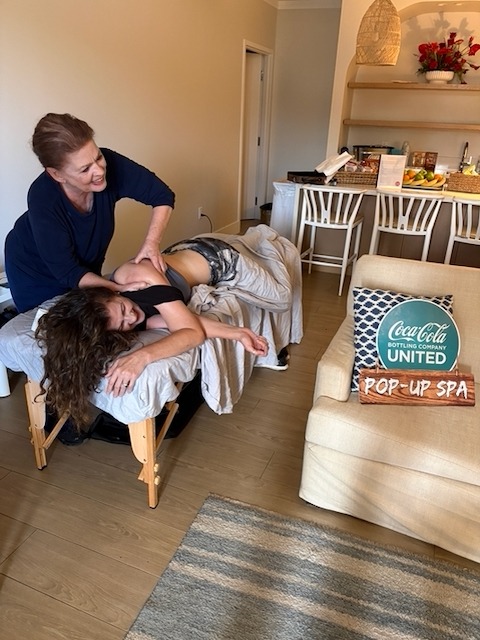 Professional massage therapist providing a shoulder treatment at a Coca-Cola United pop-up spa event.