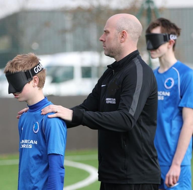 Coach standing on an outdoor football pitch with hands placed gently on a player’s shoulders