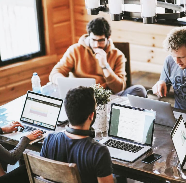 a group of people sitting around a table with laptops
