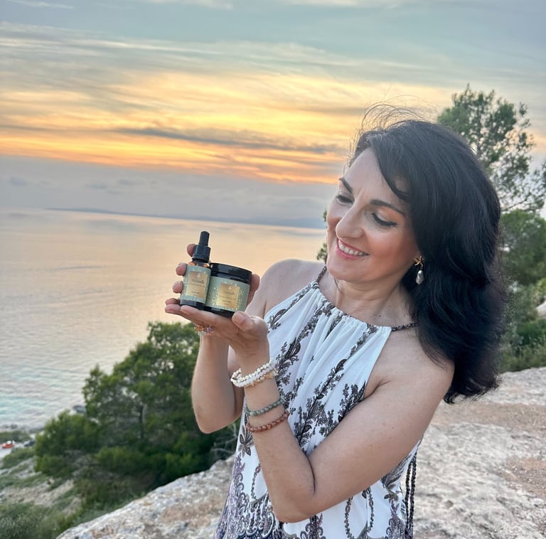 A woman holds natural organic skincare products during a scenic sunset over the Mediterranean ocean.