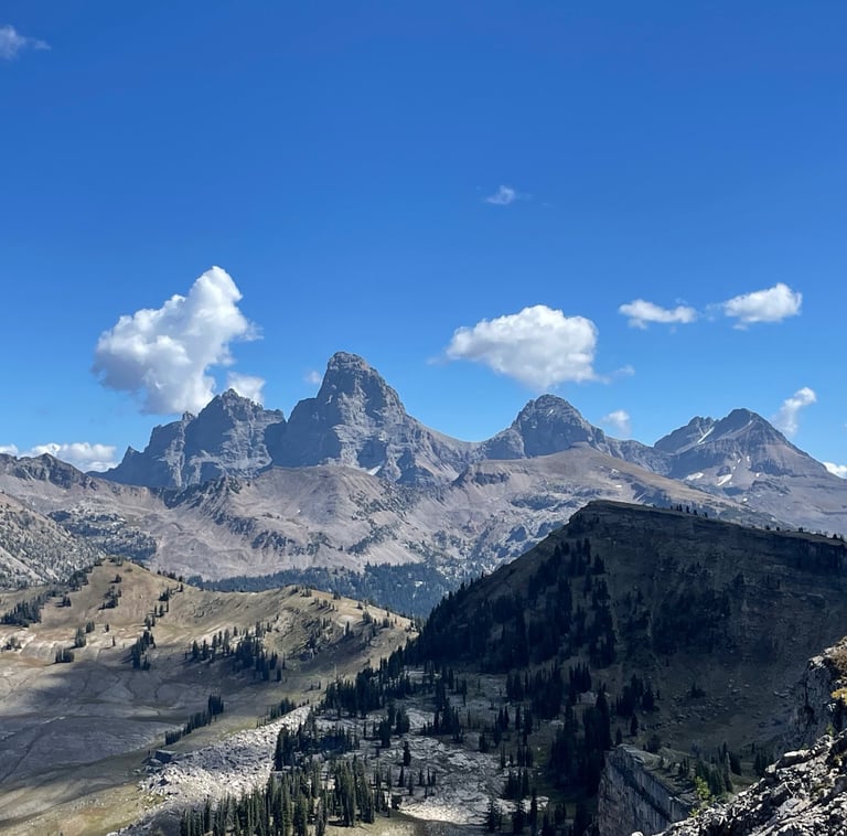 Panoramic view of the Grand Tetons mountain range with rugged peaks under a blue sky with fluffy clouds.