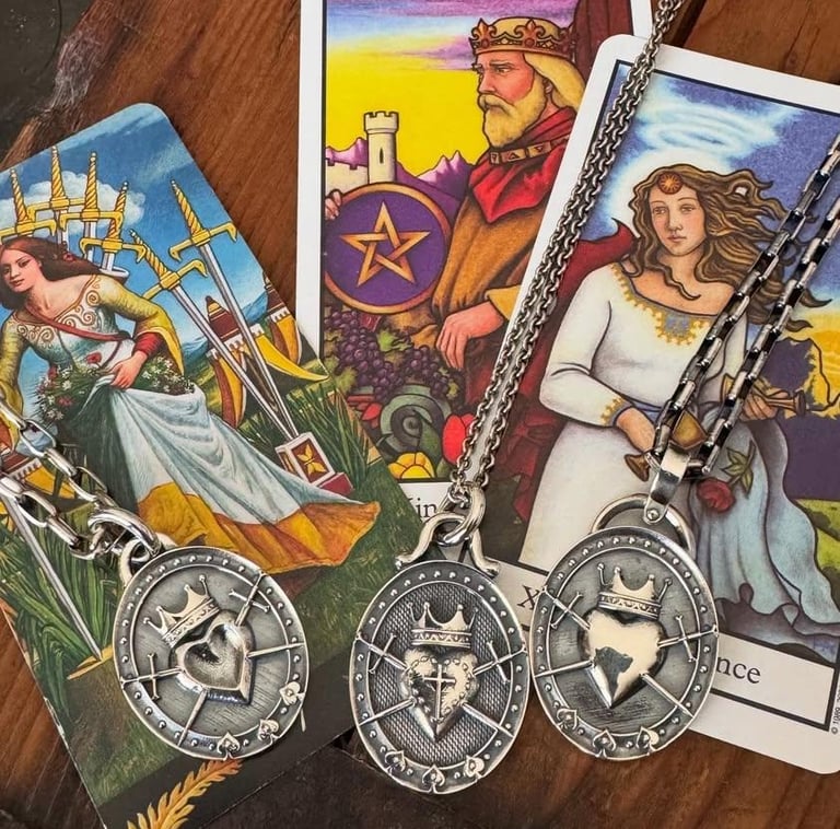 Three silver crowned heart pendants on chains resting on tarot cards with spiritual imagery.