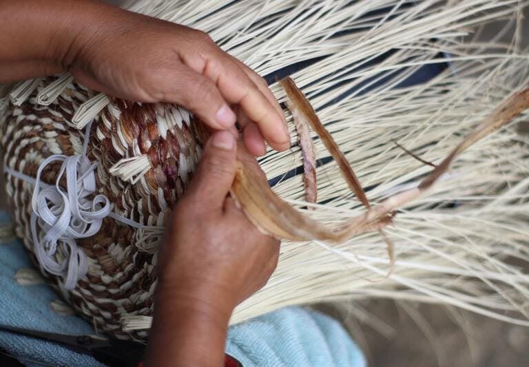 Persona tejiendo canasta con fibras naturales